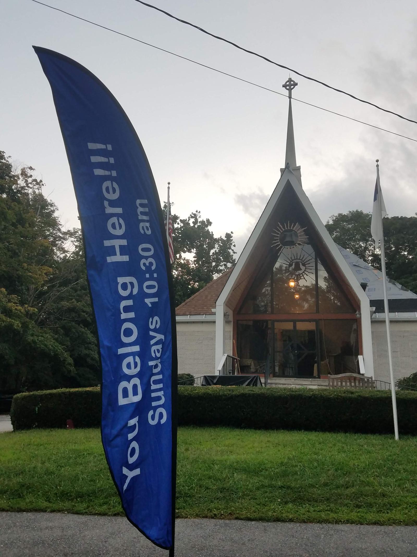 The church on Route 22 with a blue banner reading “You Belong Here! Sundays 10:30 am”